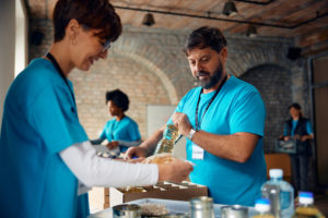 Mature Man Packing Donation Boxes While Working As Volunteer At Food Bank. - SQUIPP CONSULTORIA E ASSESSORIA CONTÁBIL